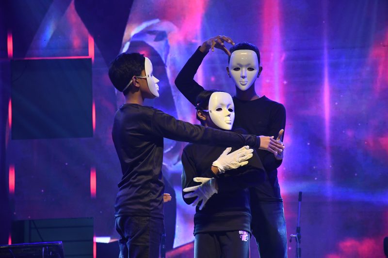 Students in white masks performing a mime on stage